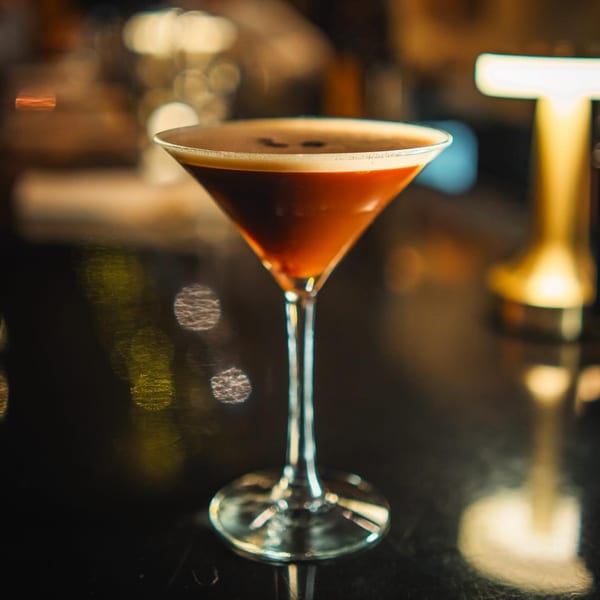 Espresso martini in a stemmed glass with coffee beans on top, on a dark bar.