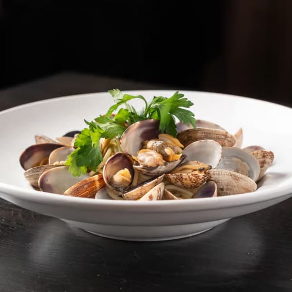 A white bowl of Gabagool Wine Bar's clams with pasta and fresh parsley on a dark surface.
