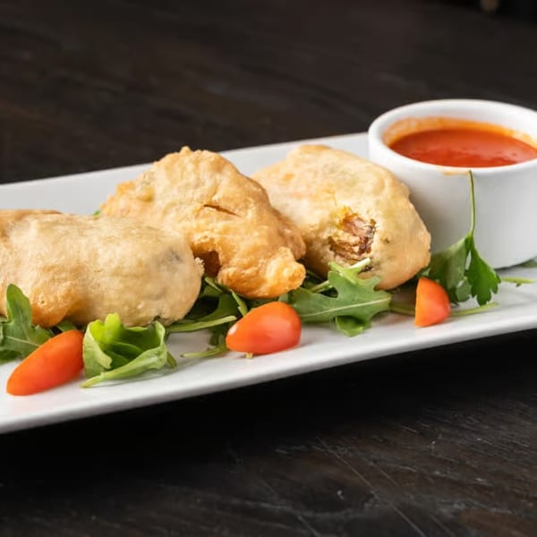 Fried appetizers with a side of red dipping sauce, garnished with arugula and cherry tomatoes.