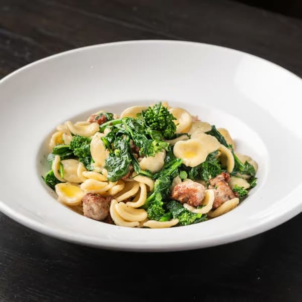 Orecchiette pasta with broccoli rabe and sausage in a white bowl on a dark table.