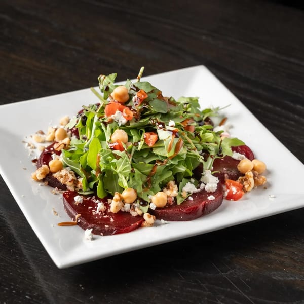 Beet salad with arugula, chickpeas, walnuts, feta, and balsamic glaze on a white plate.