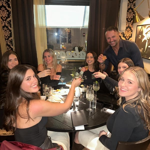 Friends at Gabagool Wine Bar raising glasses for a toast around a dark round table.