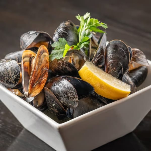 Steamed mussels in a white bowl, garnished with parsley and a lemon wedge.