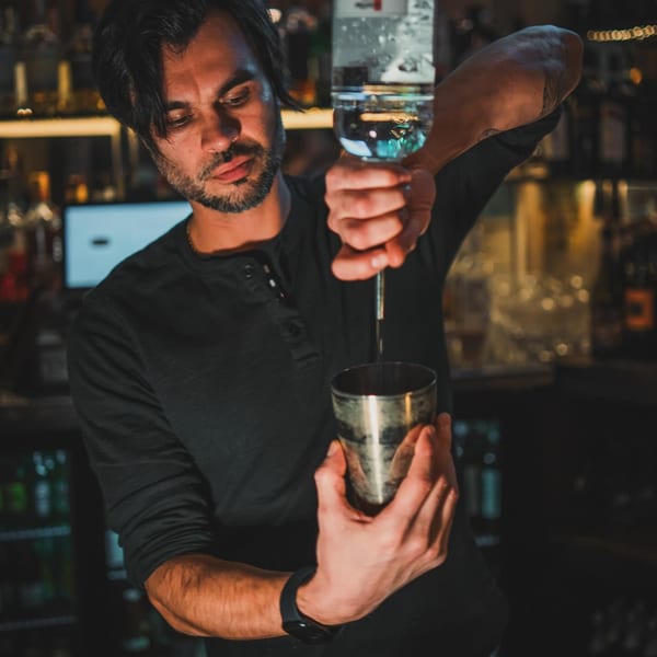 A bartender at Gabagool Wine Bar pours liquor from a bottle into a metal shaker.