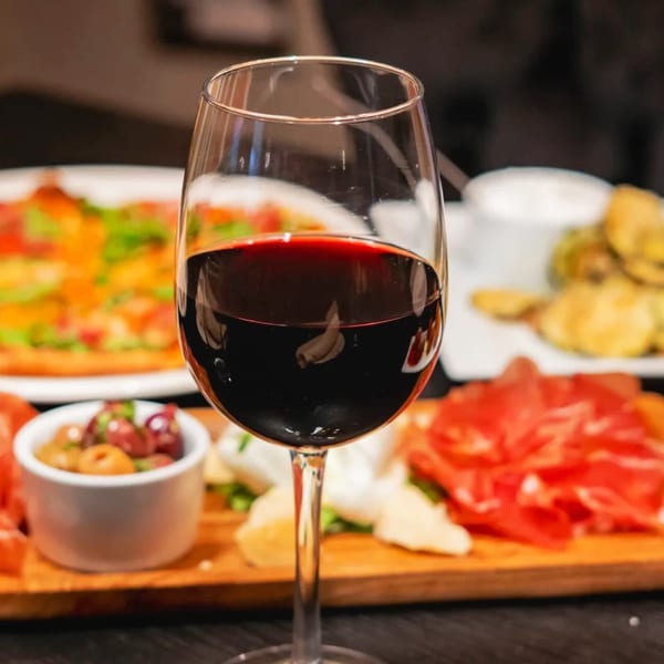 A glass of red wine sits in front of a charcuterie board and pizza at Gabagool Wine Bar.
